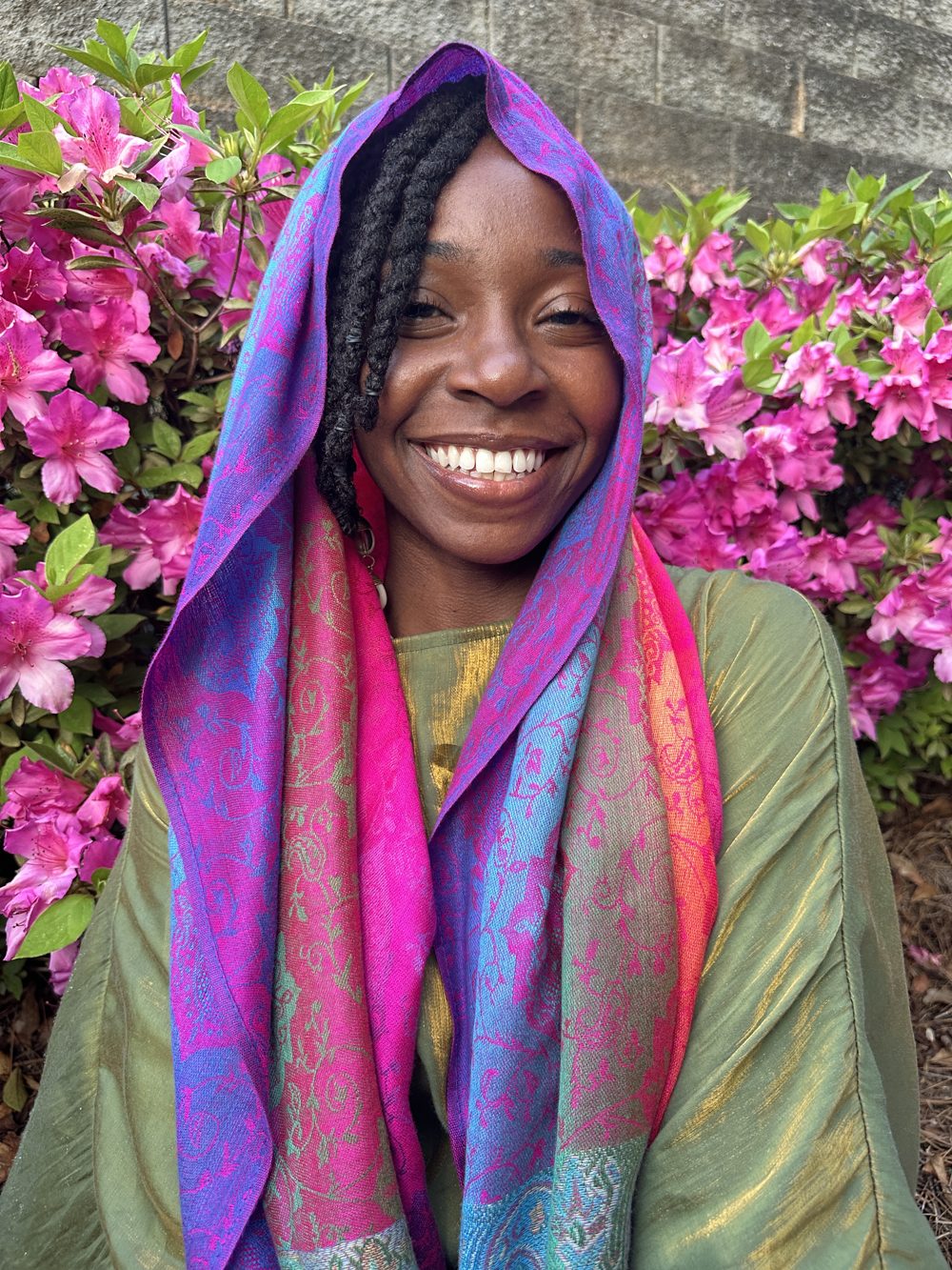 Kait smiling in a violet and magenta scarf in front of pink azaleas